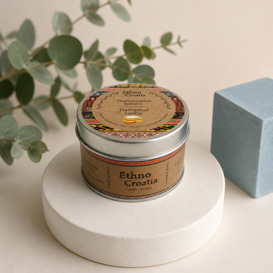 Scented Candle – Traditional Cookie (Ethno Croatia) Tin of 'Ethno Croatia' cookies on a white pedestal with a plant and blue block in the background. snc shopncro