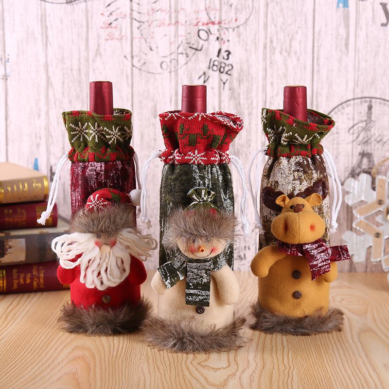 Christmas Bottle Cover – Santa, Snowman & Reindeer Three decorative bottle covers shaped like Santa Claus, snowman, and reindeer on a wooden surface.