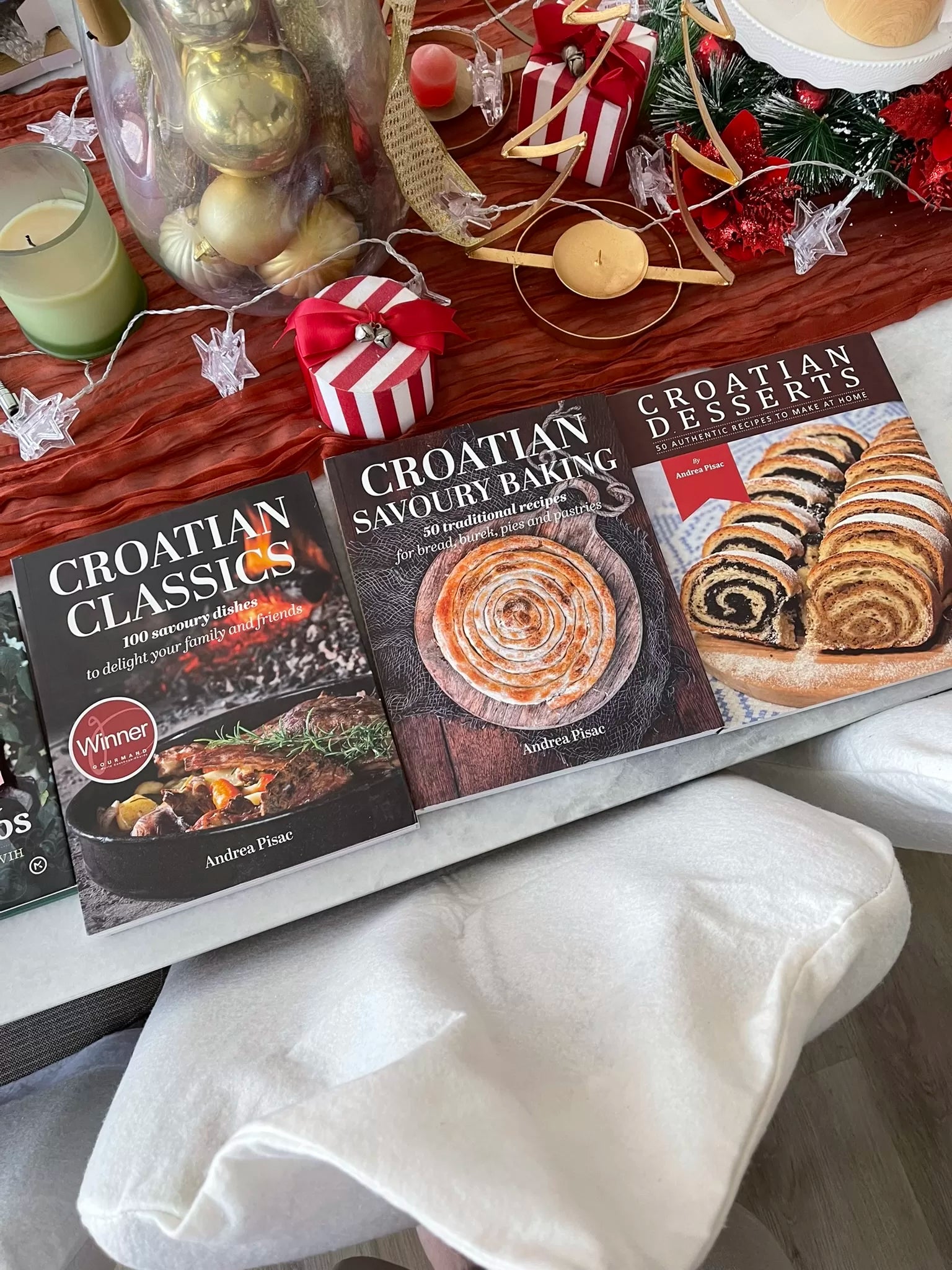 Croatian Savoury Baking: Cookbook in English Language Three cookbooks titled 'Croatian Classics', 'Croatian Savoury Baking', and 'Croatian Desserts' on a table with festive decorations.