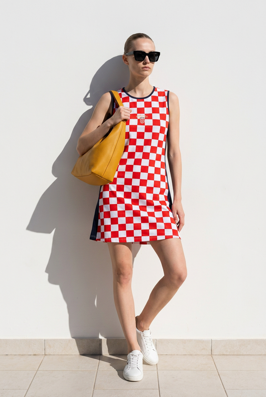 Dress Croatia Checks (shorter) Woman wearing a red and white checkered dress with sunglasses and a yellow bag against a white wall.