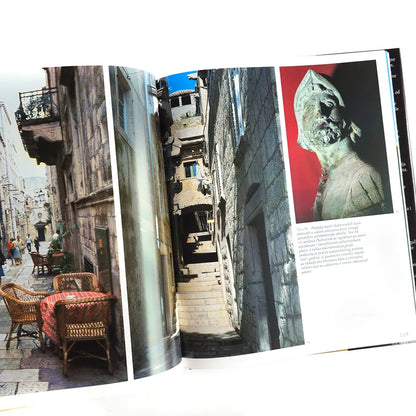 Hrvatska - Photographic Monograph Open book showing images of a narrow street with people, a statue, and a table with chairs.
