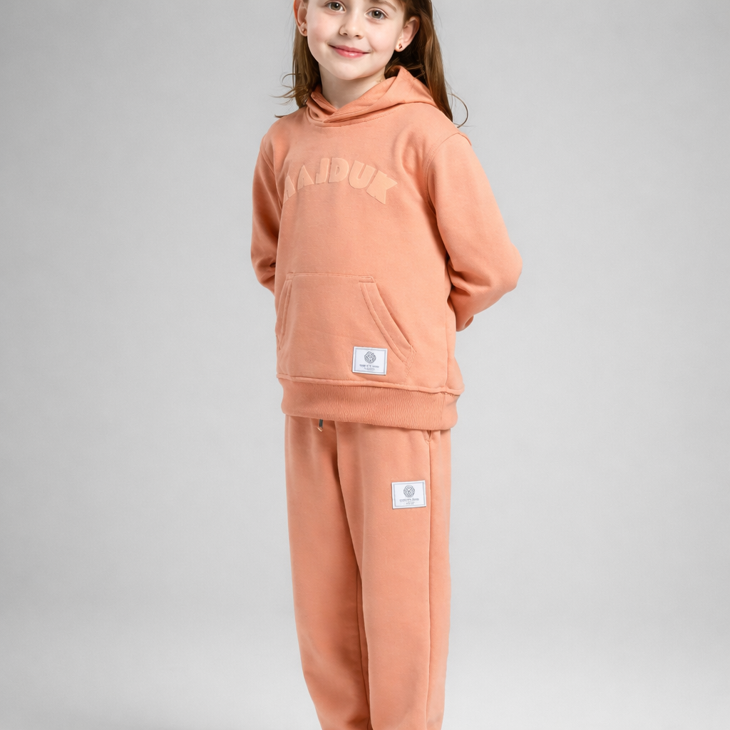 Child wearing a peach-colored hoodie and pants set on a gray background Kids Tracksuit Hajduk
