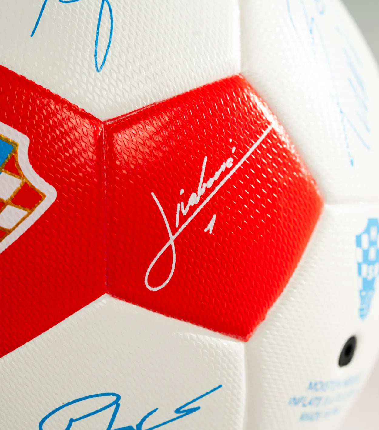 Close-up of a soccer ball with red and blue signatures on a white background