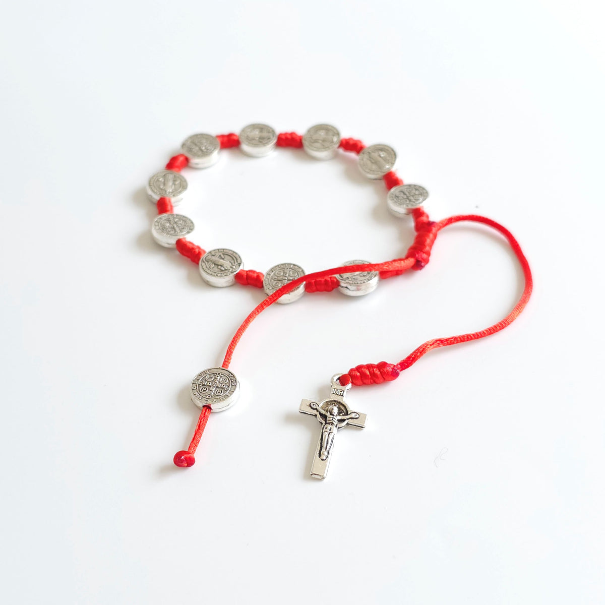 Saint Benedict Adjustable Bracelet with Cross (Red) Red cord bracelet with silver charms on a white background