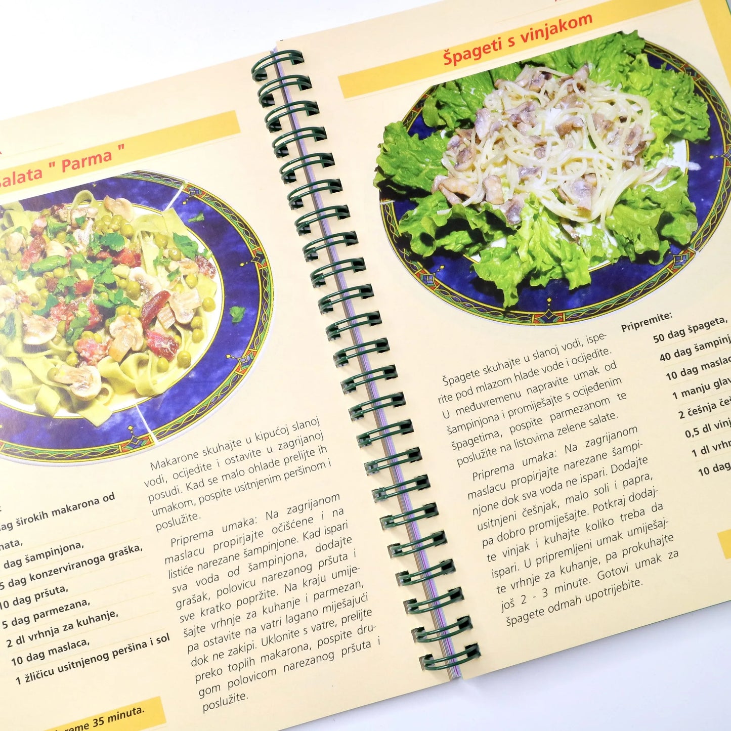 Salate - Prilog, Jela i Desert Open cookbook showing a page with spaghetti and broccoli dish and another dish on a blue plate.