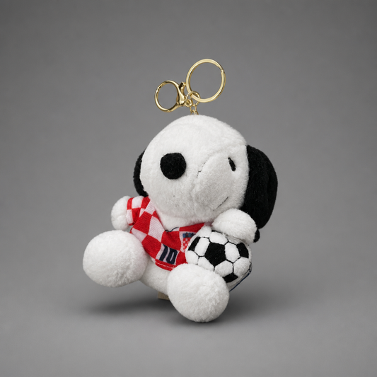 A plush Snoopy keychain wearing a red and white checkered soccer jersey and holding a black and white soccer ball, attached to a gold metal key ring, set against a solid gray background. Singing Croatian Fan Puppy – Hanging Plush Toy