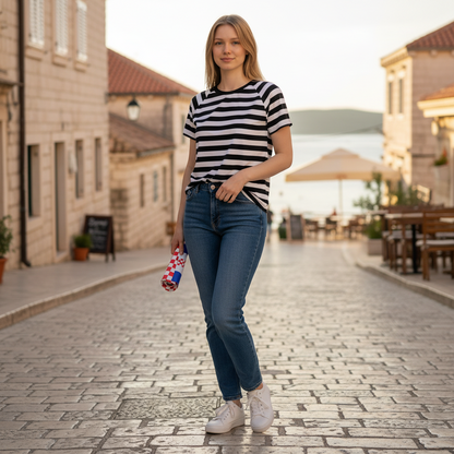 T-shirt Dalmatia Boat Neck Woman in a striped shirt and jeans standing on a cobblestone street.