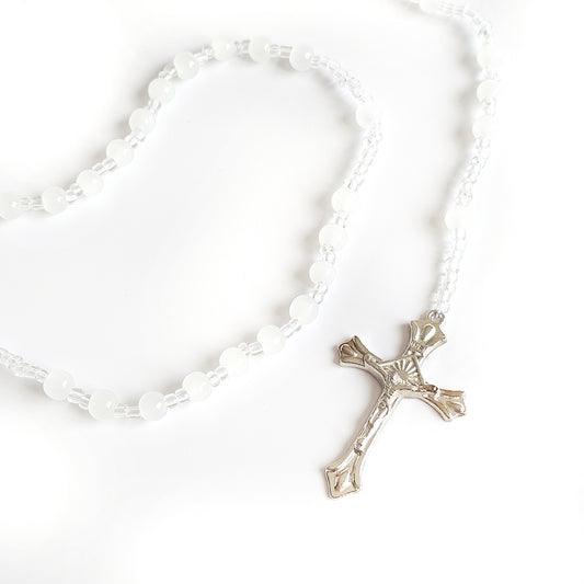 White Bead Catholic Rosary – Silver Crucifix Silver cross pendant on a white beaded necklace against a white background