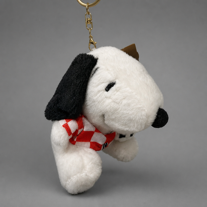 A plush Snoopy keychain charm featuring the character in a white and black color scheme, wearing a red and white checkered scarf, suspended from a gold metal key ring against a neutral gray background. Singing Croatian Fan Puppy – Hanging Plush Toy